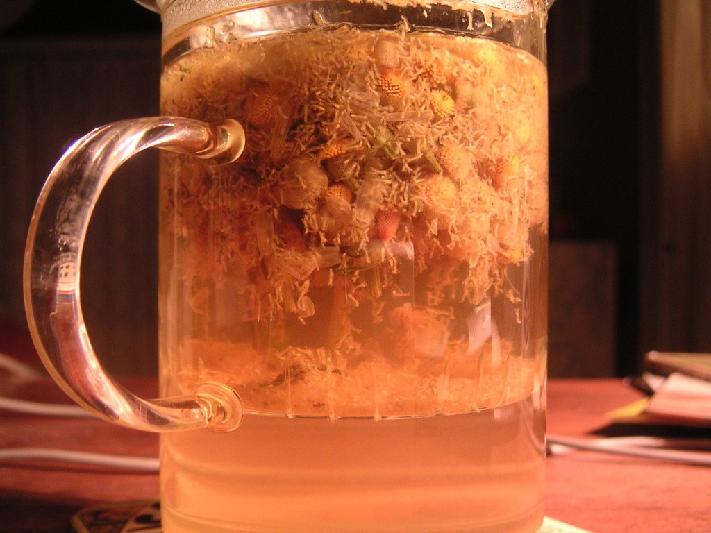 A clear glass of golden chamomile tea brewed from dried flowers